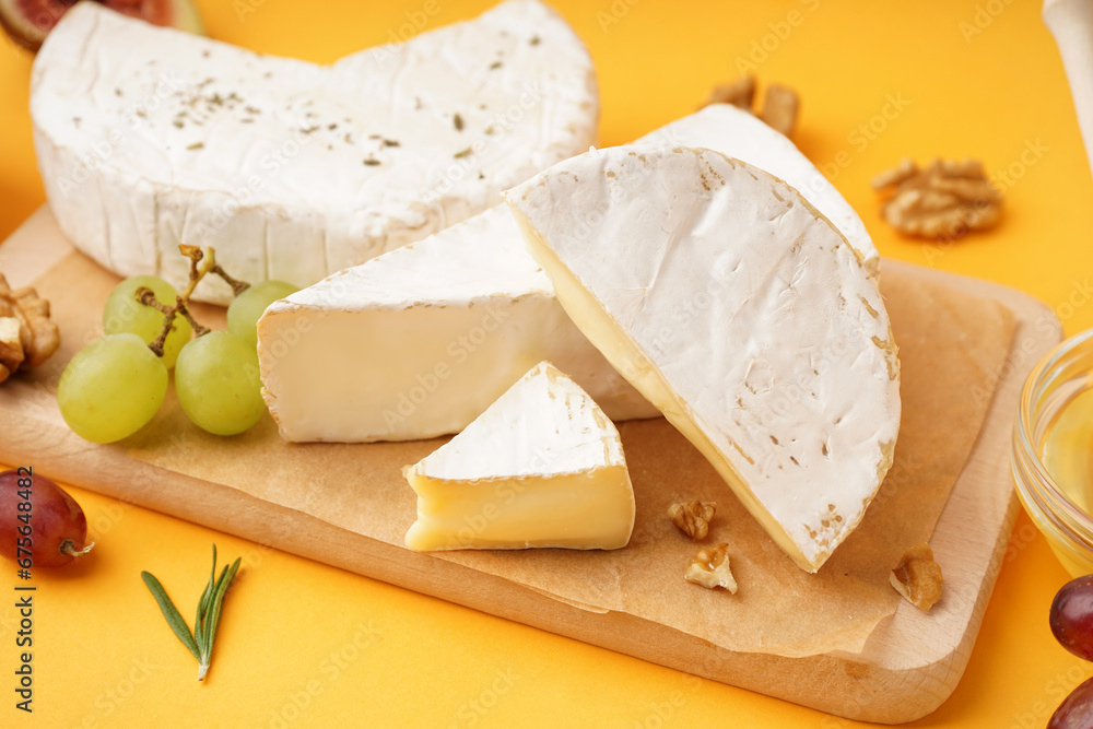 Wooden board with pieces of tasty Camembert cheese on yellow background