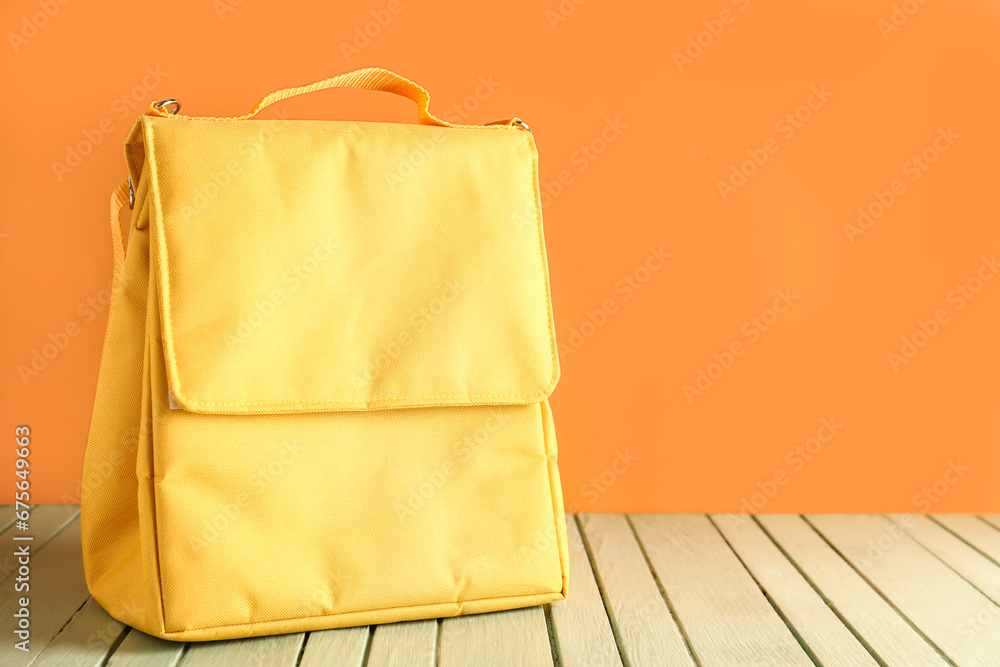 Yellow lunch box bag on green wooden table near orange wall