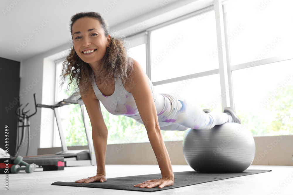 Beautiful adult woman exercising with fitness ball at gym