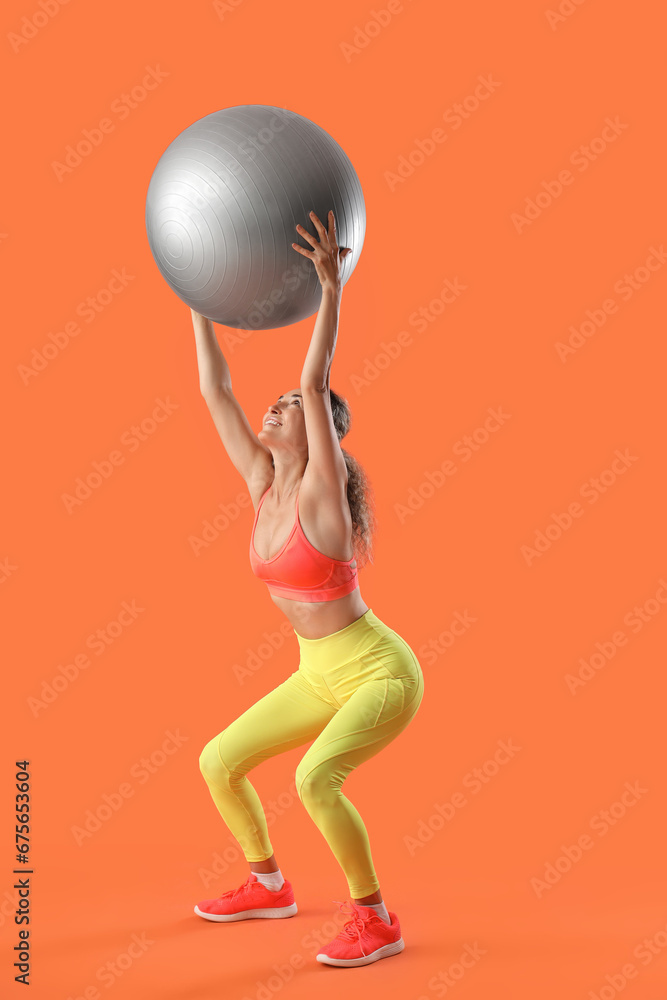 Beautiful adult woman exercising with fitness ball against orange background