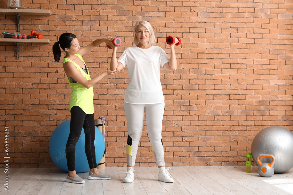 Mature woman training with dumbbells and therapist in rehabilitation center