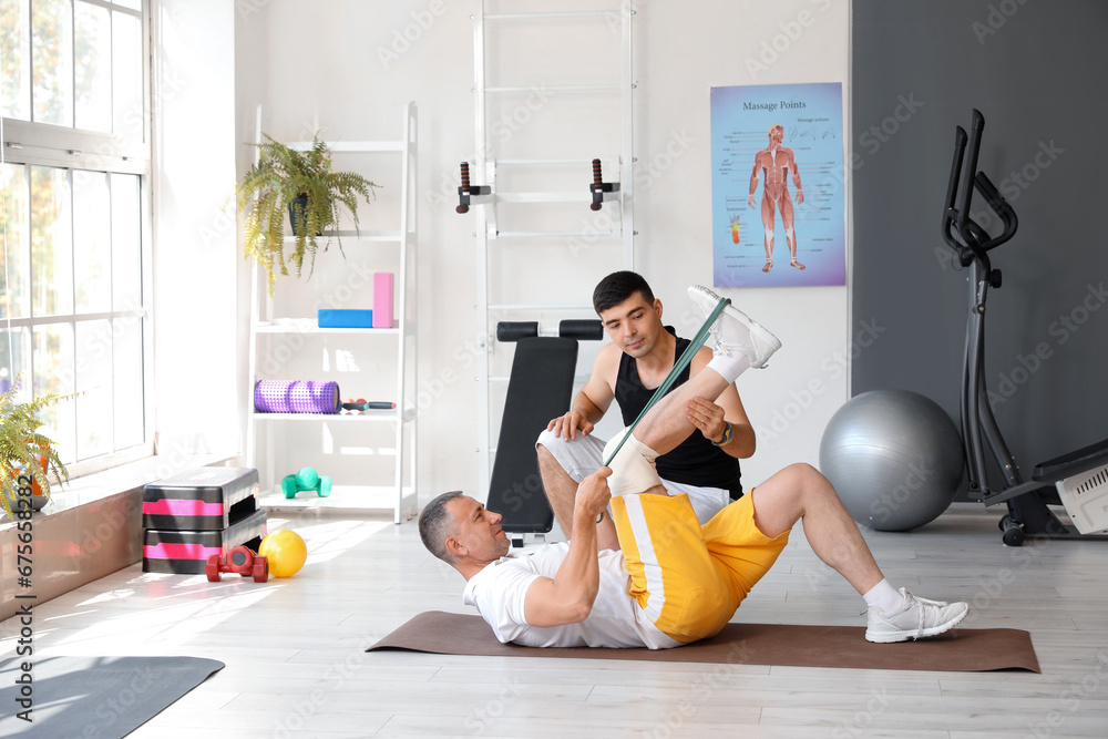 Mature man training with stretching tape and therapist in rehabilitation center