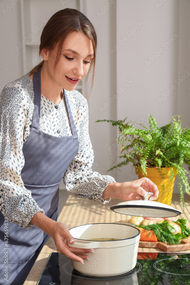 Young woman cooking chicken soup on stove in kitchen