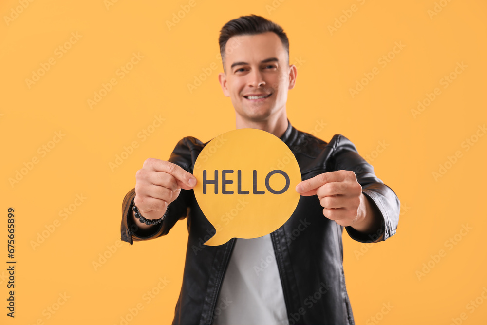 Young man holding paper speech bubble with word HELLO on yellow background