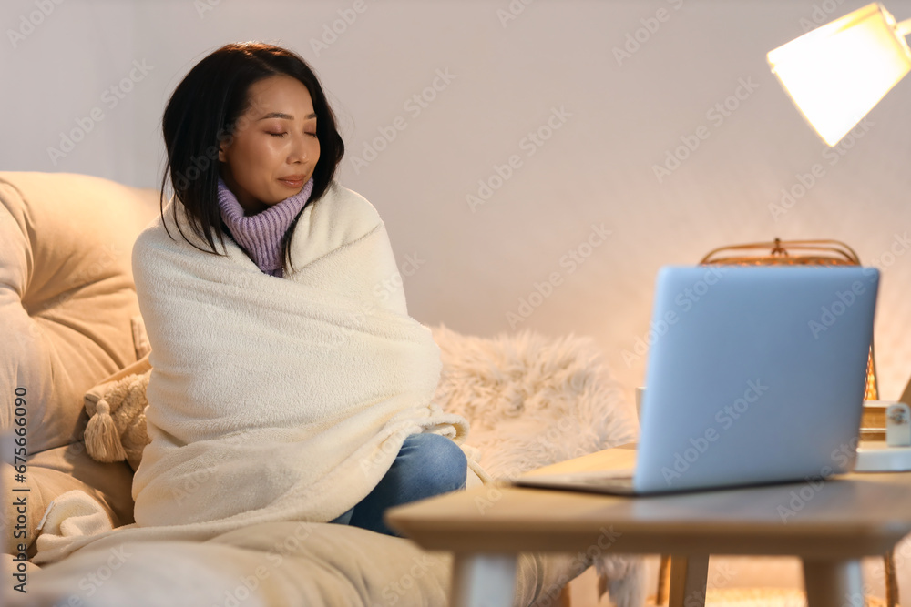 Young Asian woman with warm plaid at home in evening