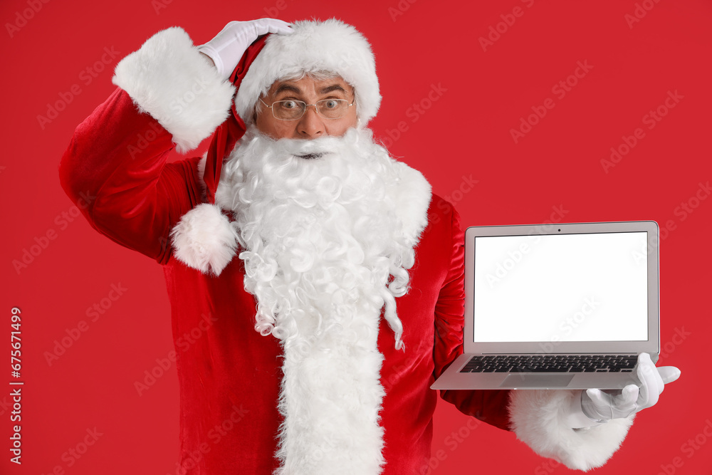 Shocked Santa Claus with laptop on red background