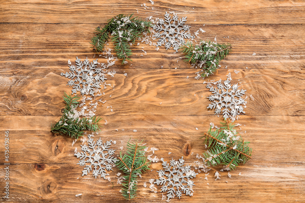 Frame made of beautiful snowflakes and fir branches on brown wooden background