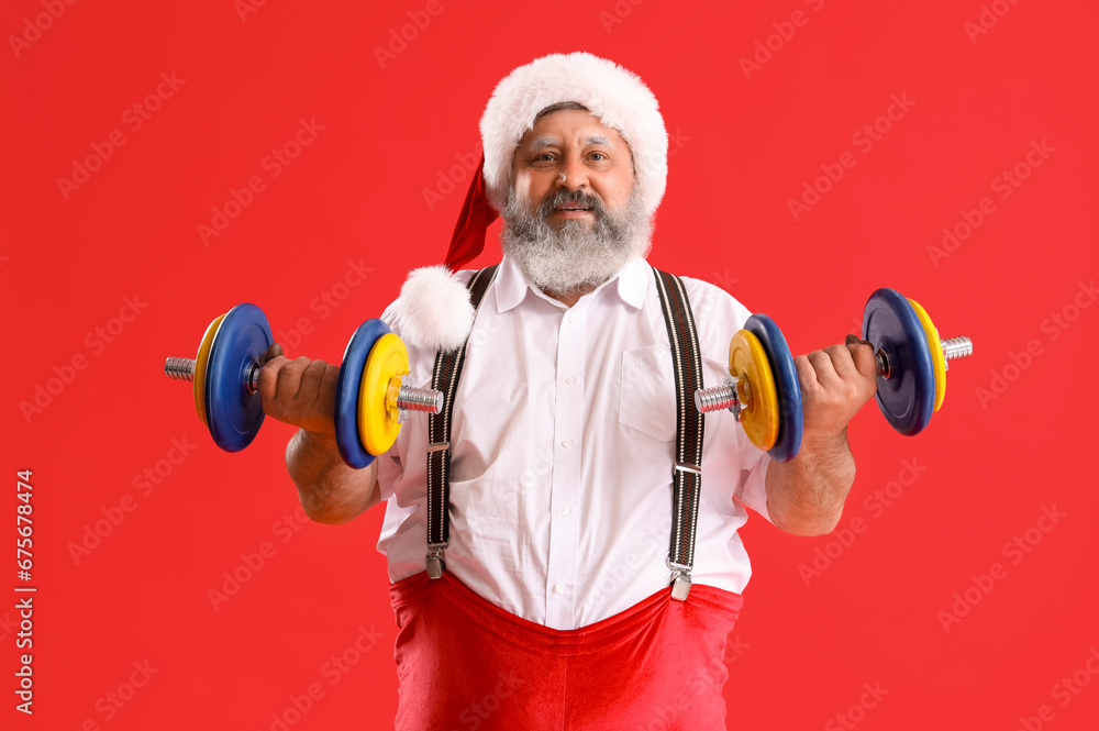 Sporty Santa Claus with dumbbells on red background