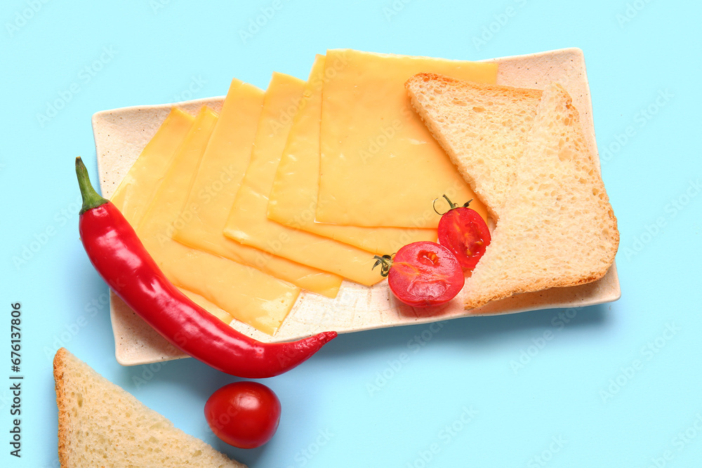 Plate of tasty processed cheese with bread and vegetables on blue background