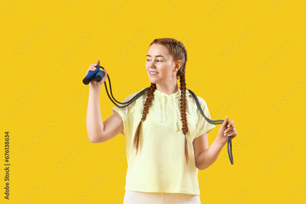 Sporty young woman with skipping rope on yellow background