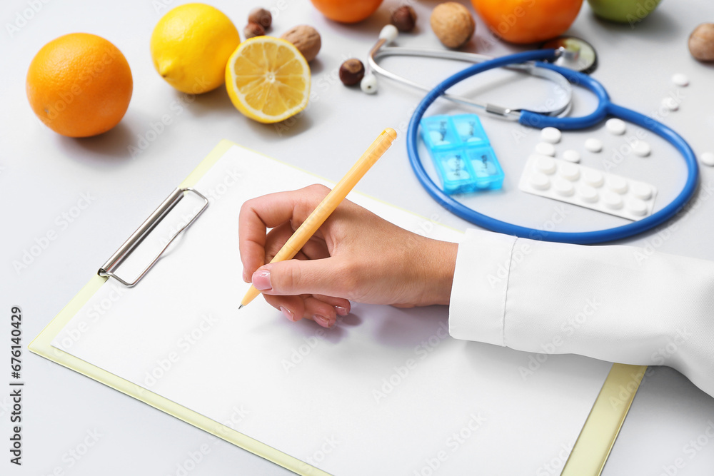 Female doctors hand with clipboard, pills and healthy products on grey background, closeup