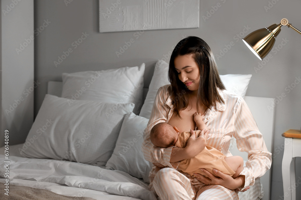 Young woman breastfeeding her baby in bedroom at night