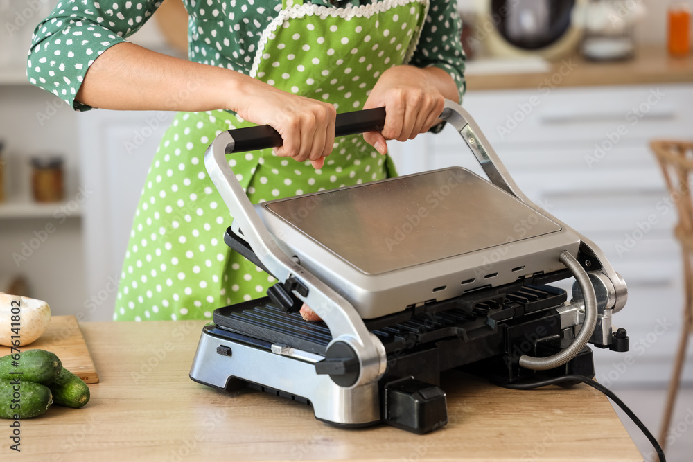 Woman cooking delicious sausages on modern electric grill in kitchen, closeup