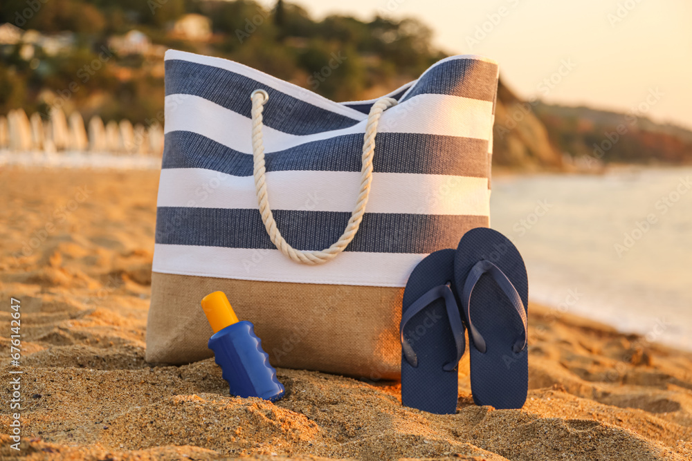 Stylish beach bag, flip-flops and sunscreen cream on sand