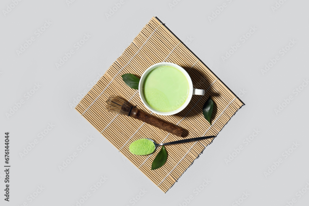 Composition with cup of fresh matcha tea, powder and chasen on grey background