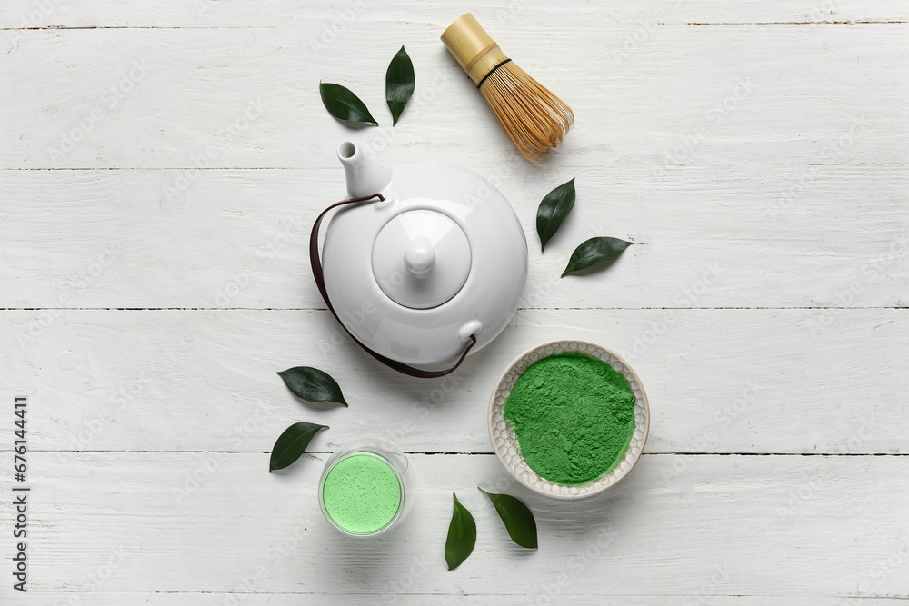 Composition with fresh matcha tea, teapot, chasen and plant leaves on light wooden background