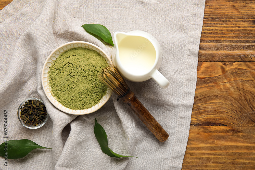 Composition with powdered matcha tea, milk and chasen on wooden background