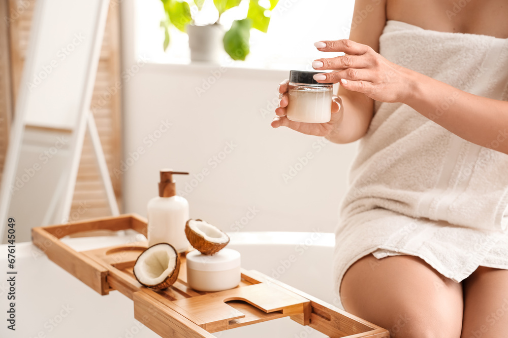 Beautiful young woman with jar of coconut oil in bathroom, closeup