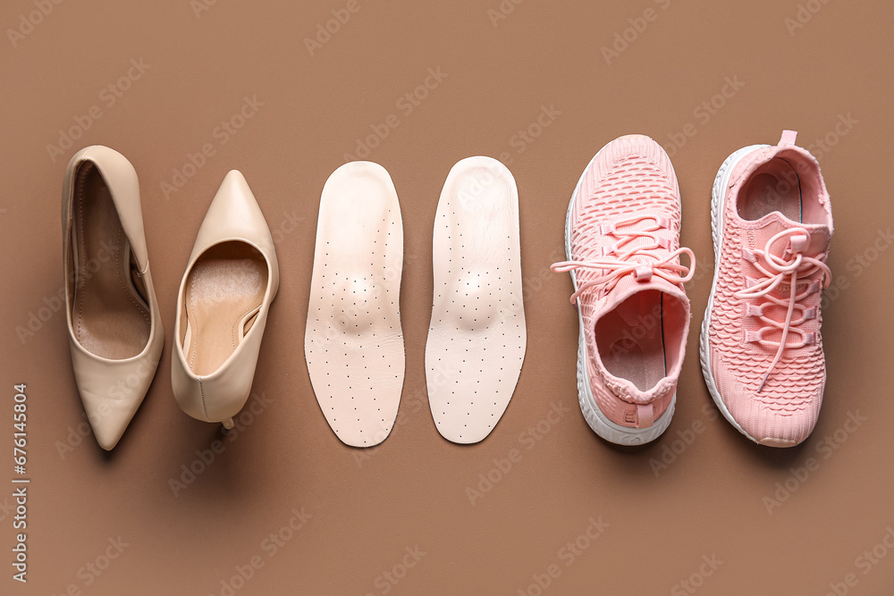 Pair of orthopedic insoles and stylish female shoes on color background