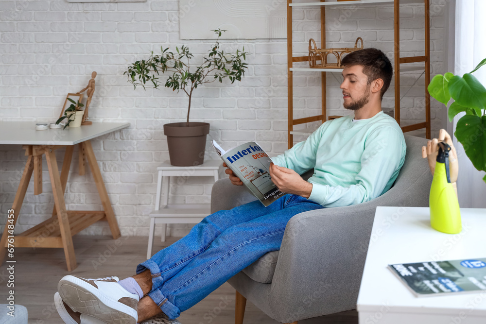 Young bearded man reading magazine in armchair at home