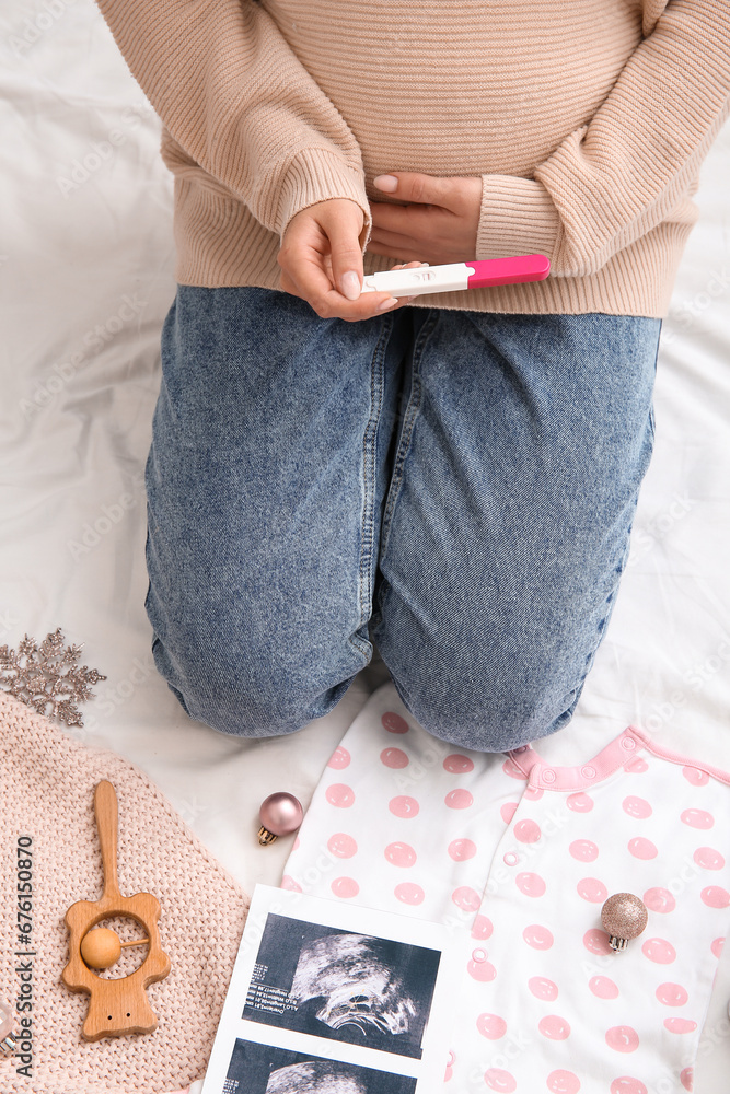 Pregnant woman with test, baby accessories and Christmas decorations on bed