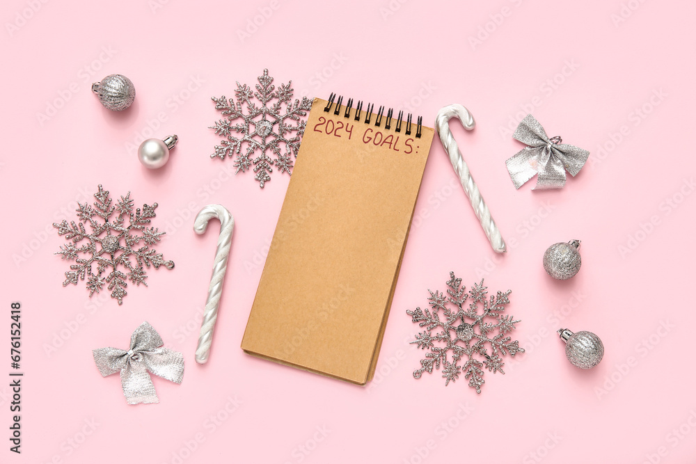 Notebook with text 2024 GOALS and silver Christmas decorations on pink background