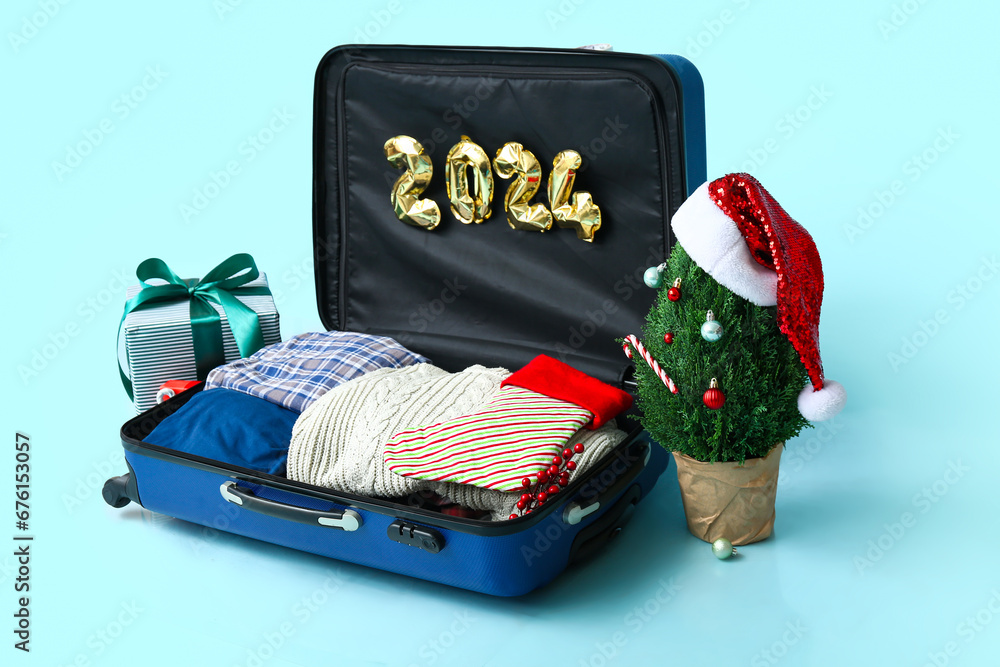 Suitcase with clothes, figure 2024 made of balloons, Christmas tree and gifts on color background