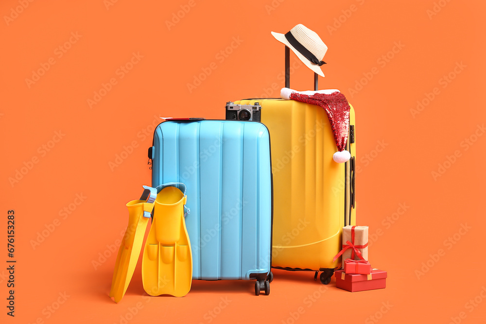 Suitcases with beach accessories, Santa hat and Christmas gifts on color background