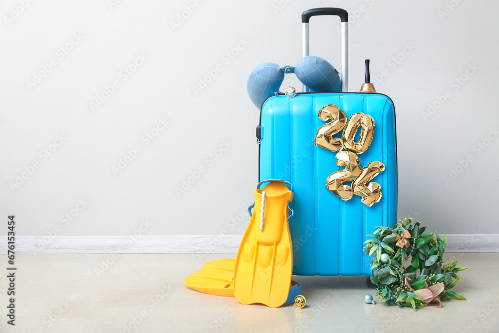 Suitcase with Christmas decorations, flippers and travel pillow near light wall in room