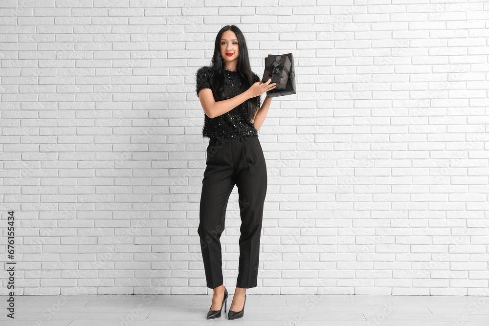 Beautiful stylish woman with gift boxes near white brick wall. Black Friday Sale