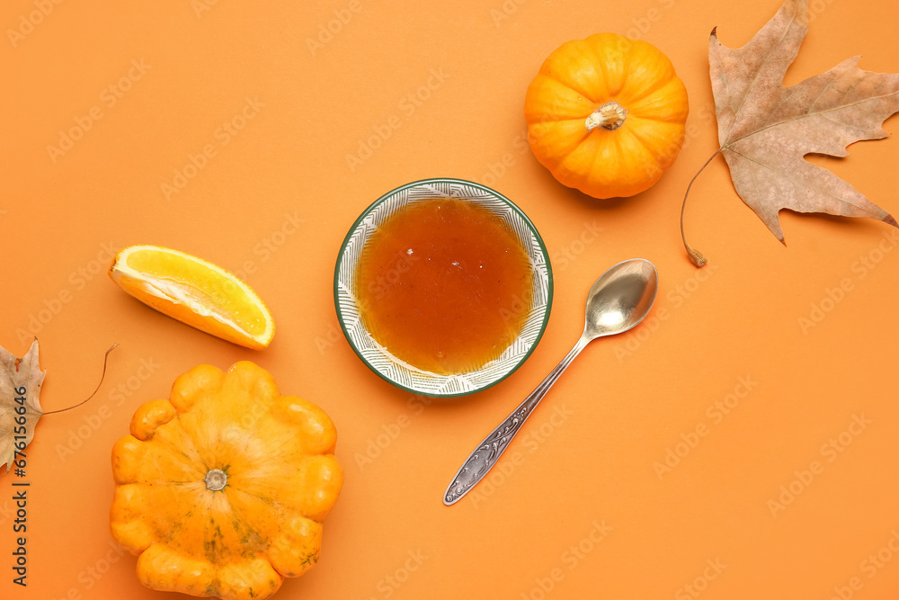 Bowl of sweet pumpkin jam with orange and autumn leaves on color background