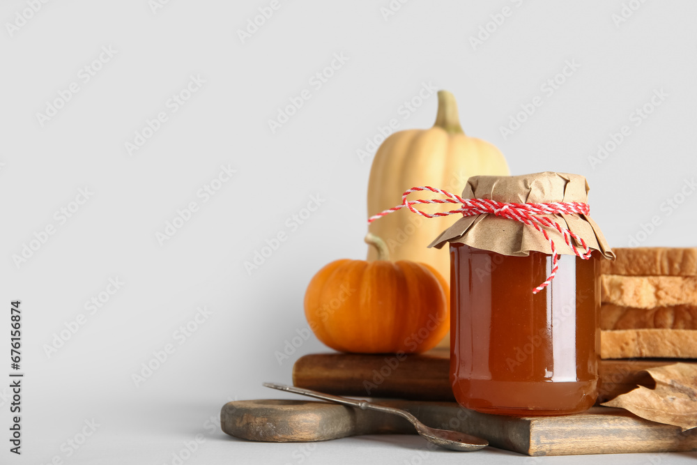 Wooden board with jar of sweet pumpkin jam and toasts on white background