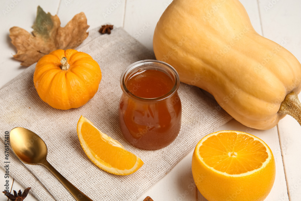 Jar of sweet pumpkin jam with orange on white wooden background