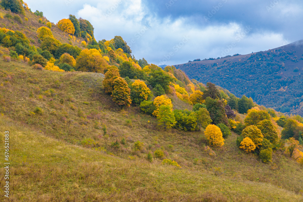 Warm autumn in the mountains covered with bright autumn trees. Colorful landscape.