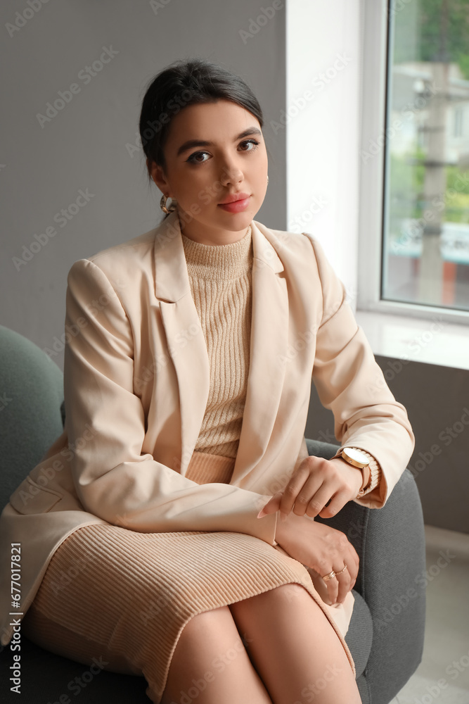 Beautiful young woman with wristwatch sitting on sofa in living room