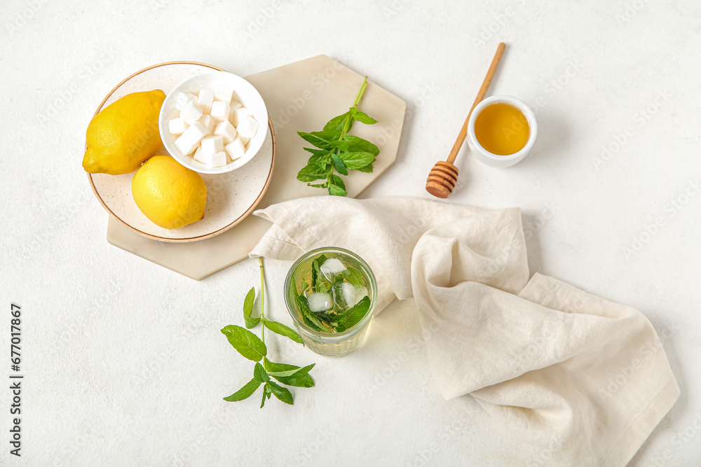 Glass of fresh icy mint tea with lemons, honey and sugar cubes on white background