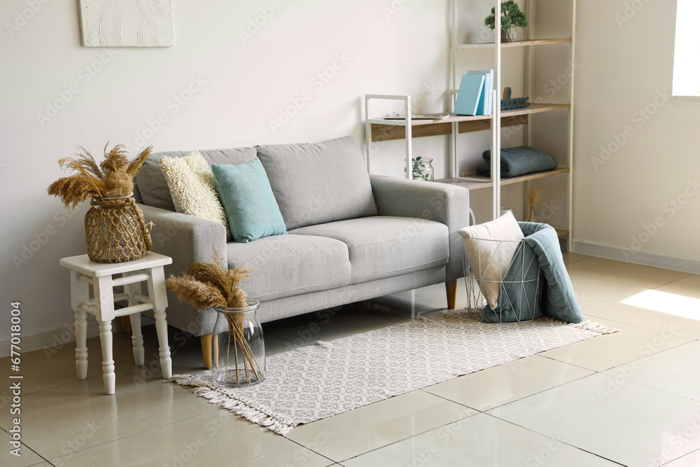 Cozy grey sofa and basket with soft blanket in interior of living room