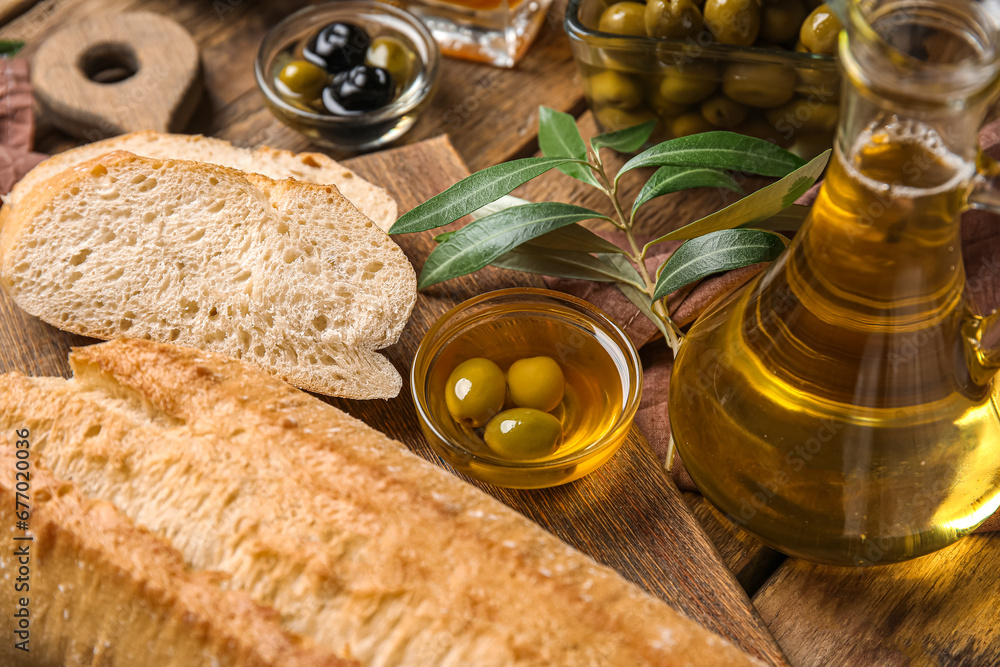 Jug and bowl of fresh olive oil with bread on wooden background