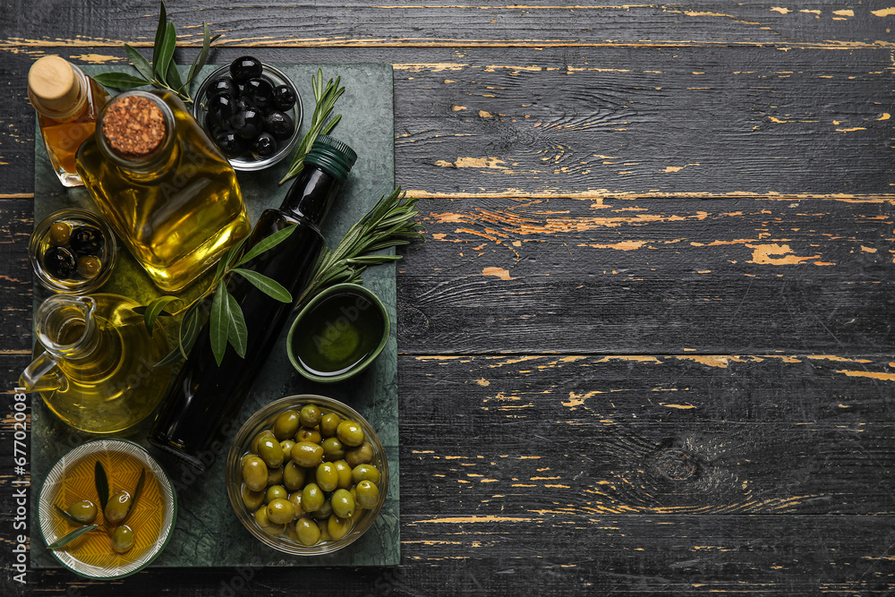 Bowls and glassware with fresh olive oil on black wooden background