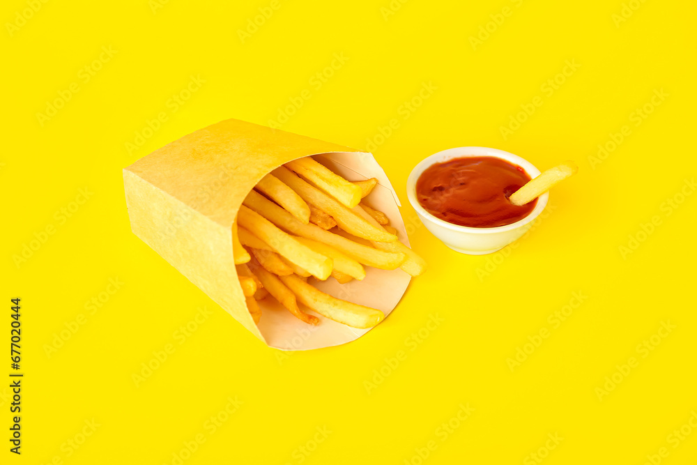 Paper box with tasty french fries and bowl of ketchup on yellow background