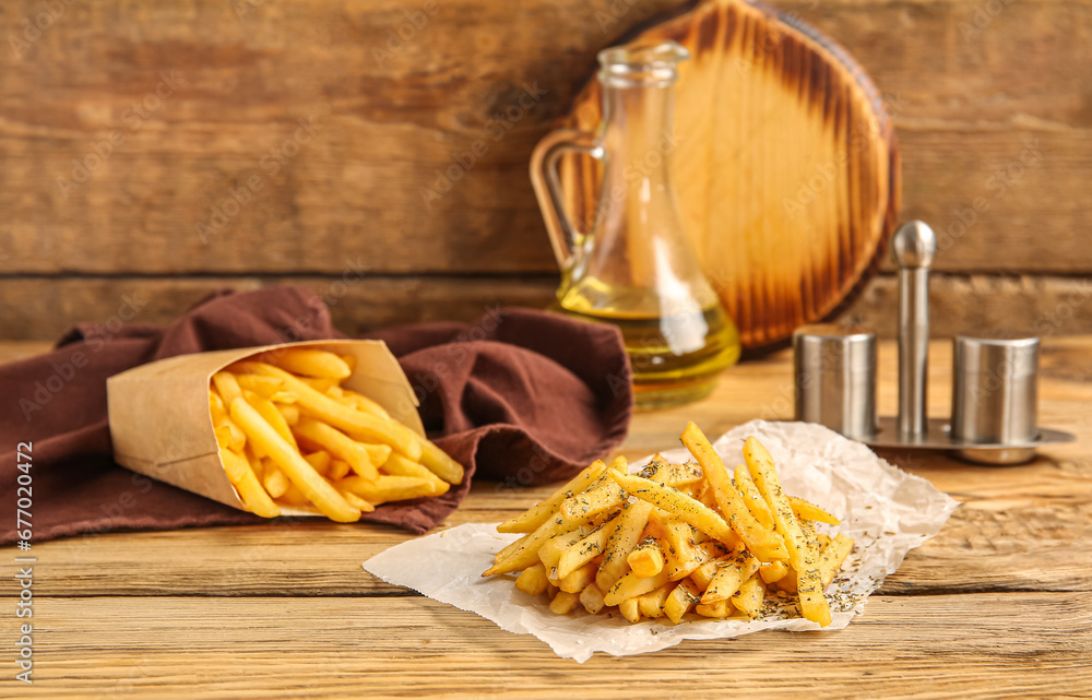 Tasty french fries with spices and oil on brown wooden background