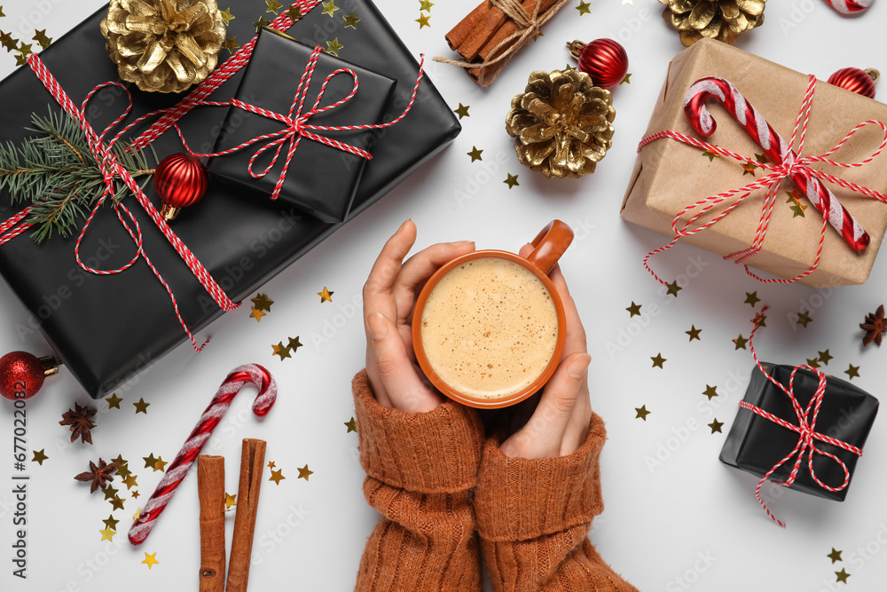 Woman with cup of coffee, gift boxes and Christmas decor on grey background