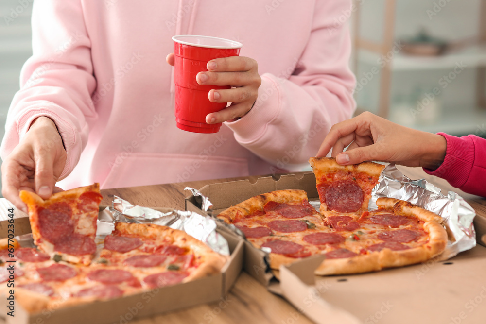 Young couple eating tasty pepperoni pizza in kitchen, closeup