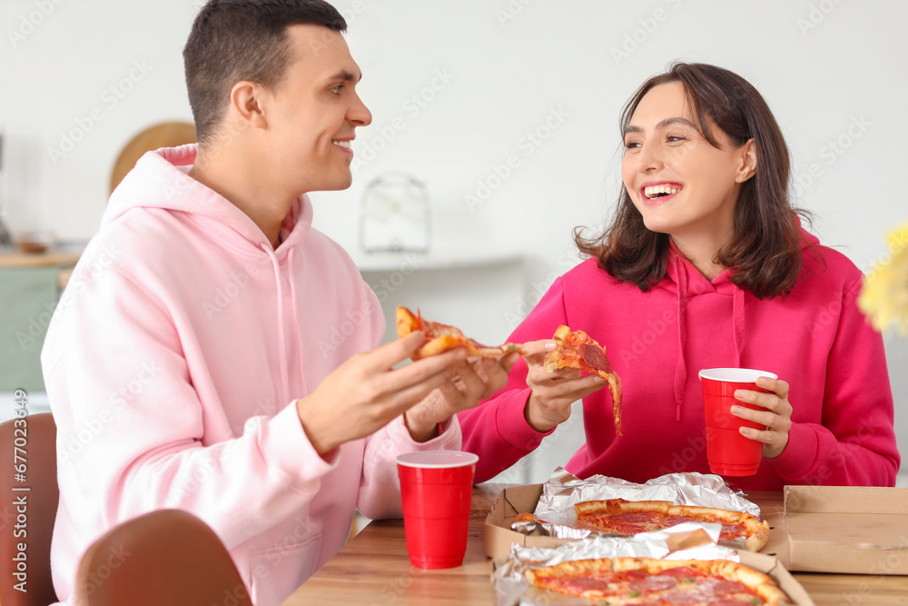 Young couple eating tasty pepperoni pizza in kitchen