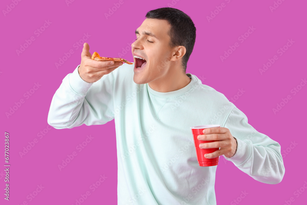 Young man with tasty pepperoni pizza and drink on purple background