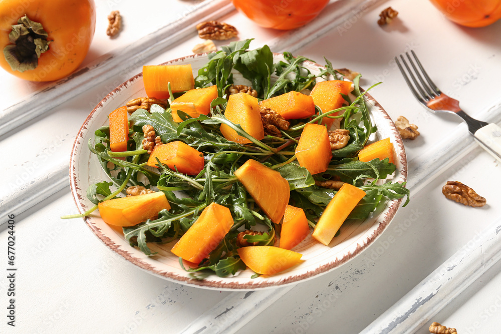 Plate of delicious salad with persimmon and walnut on white background