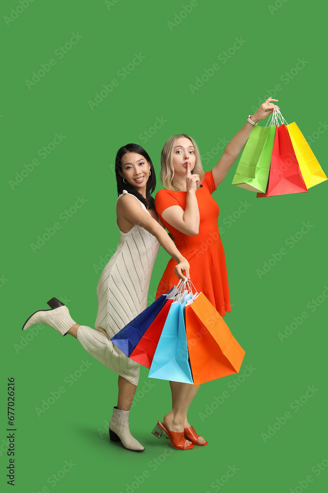 Beautiful young women with shopping bags on green background