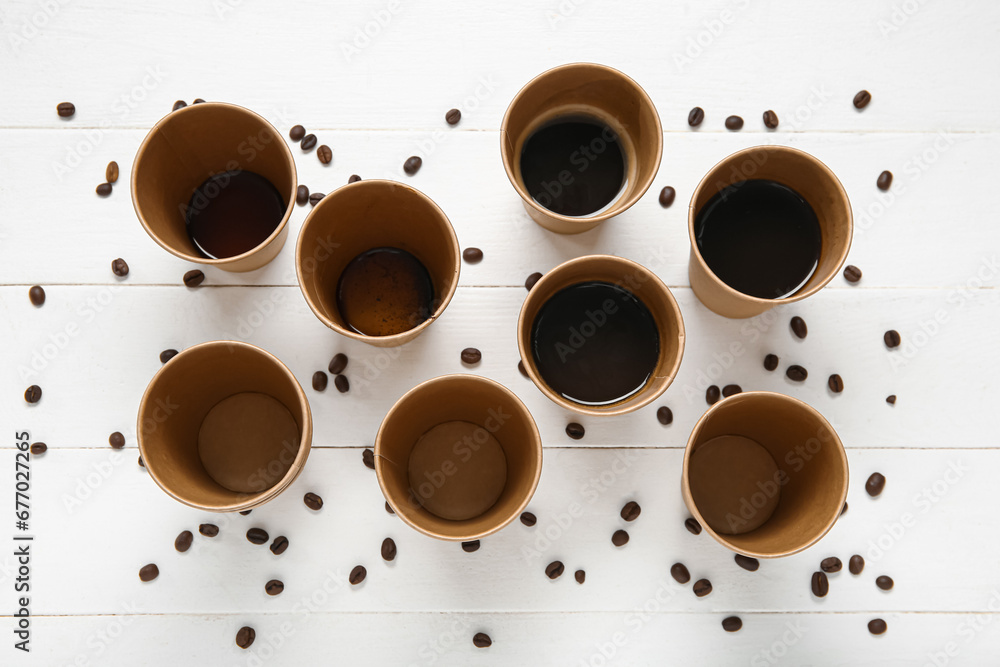 Cups of hot coffee and beans on white wooden background