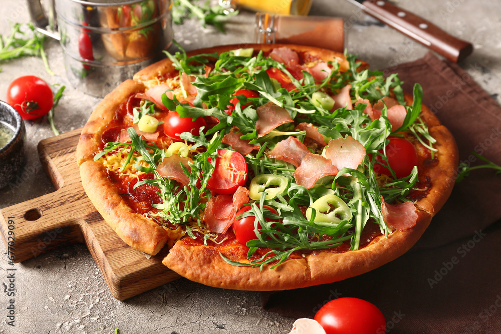 Wooden board of delicious pizza with tomatoes and arugula on grey background