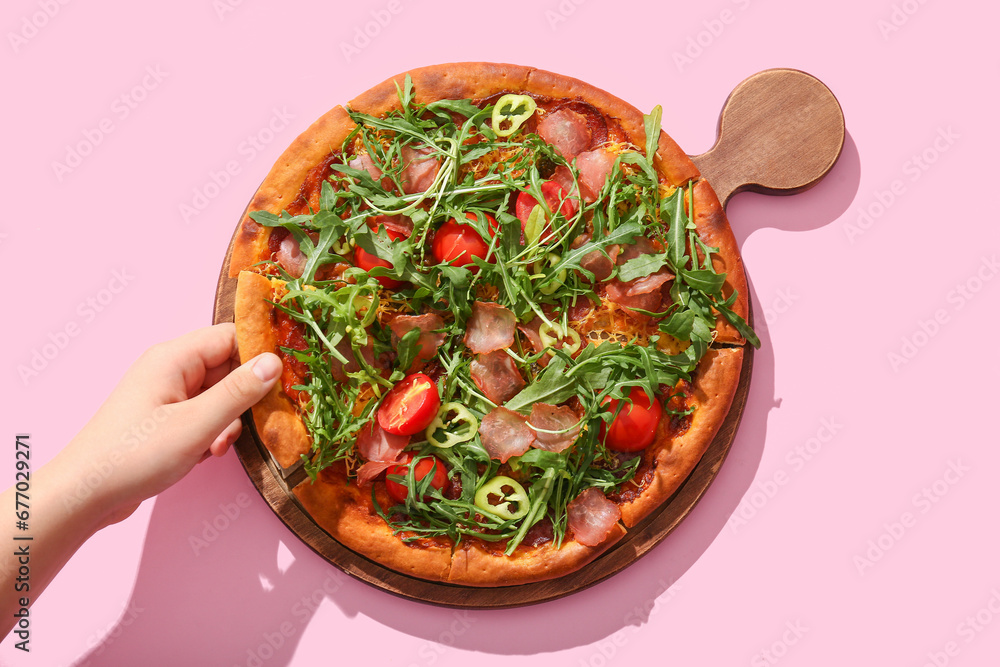 Woman taking piece of delicious pizza with tomato and arugula on pink background